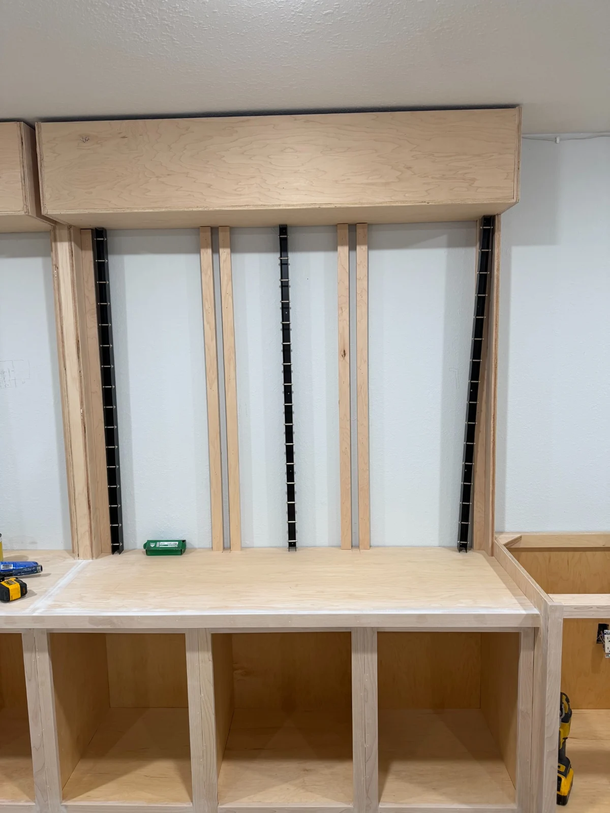Unfinished display wall with vertical mounting tracks, raw wood header and base cabinet bays