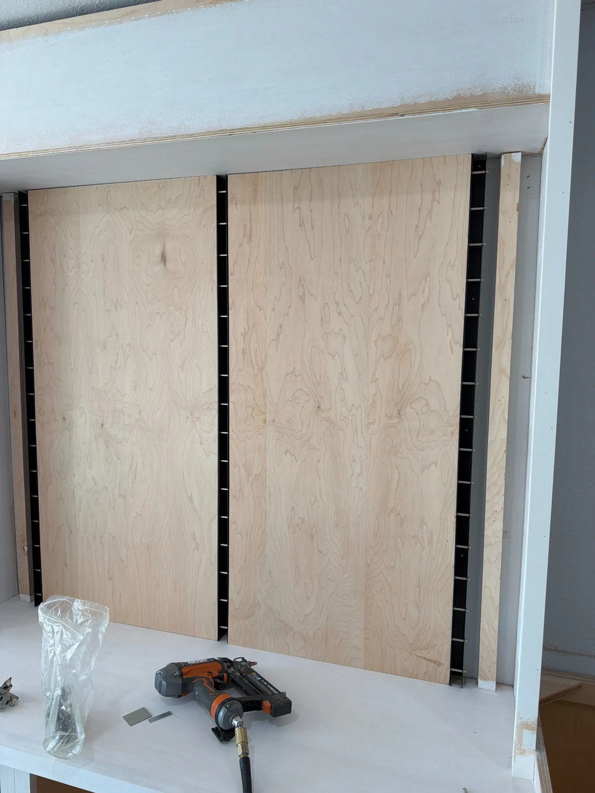 Wood display panels fitted between recessed vertical tracks beneath a framed header during installation