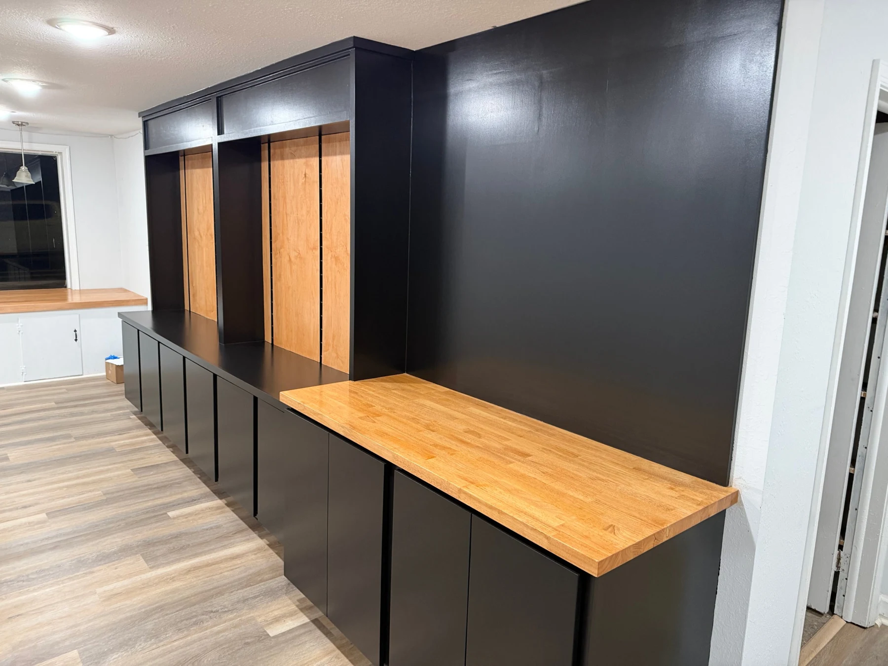 Finished display wall viewed from the side, with black cabinetry, maple display faces and the natural butcher-block counter