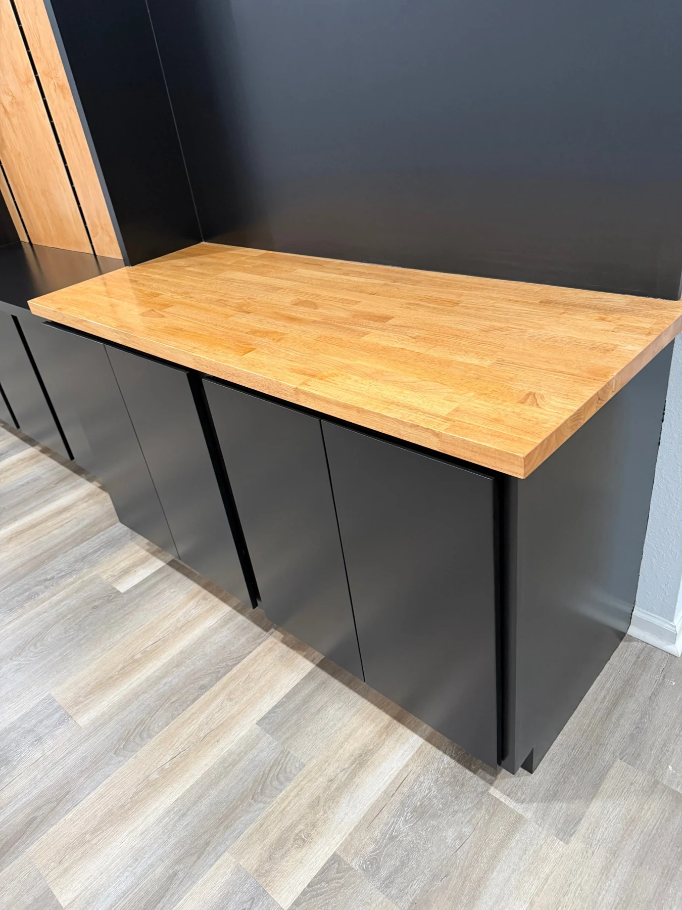 Natural butcher-block top above flat black cabinet doors with narrow reveals and no projecting handles